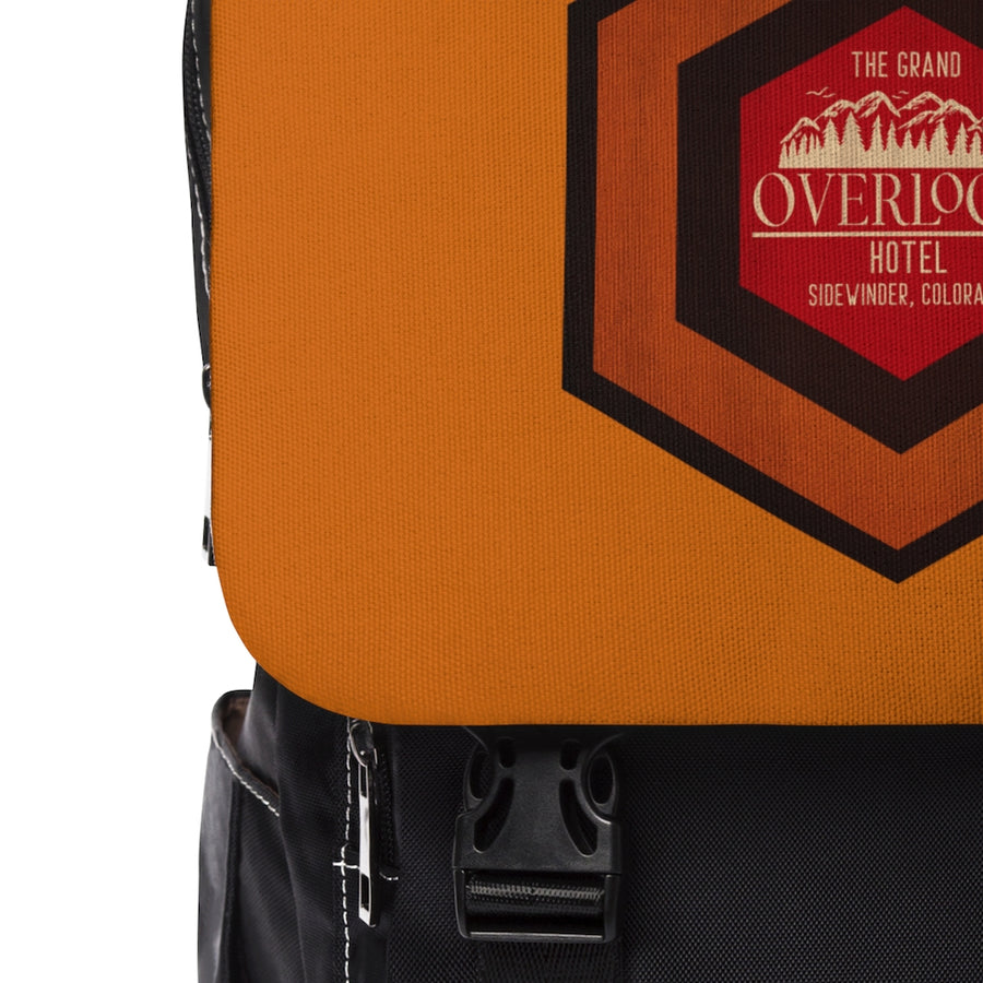 A black and brown backpack with a flap front design and a graphic on the front pocket. It has multiple compartments as indicated by the zippers and straps.